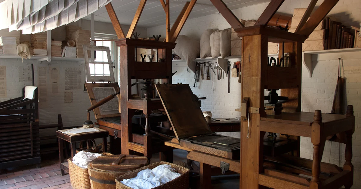 Eighteenth-century printing press with drying newspapers and rag supply.